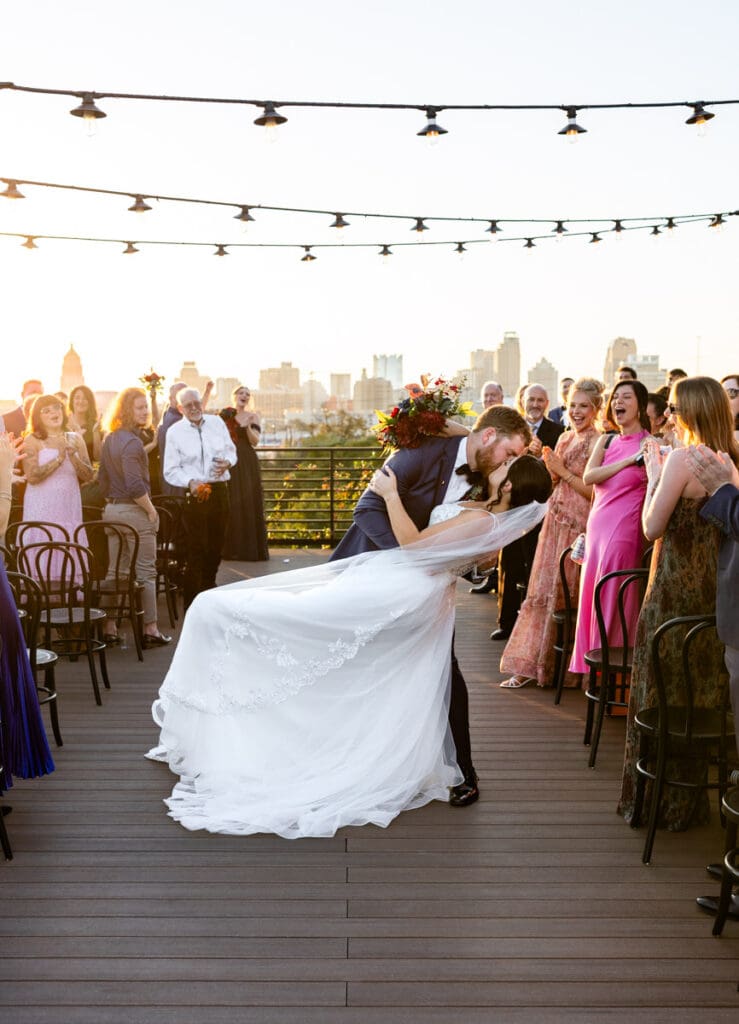 Bride and groom dip kiss during rooftop ceremony at The Skyline San Antonio with guests and downtown skyline in the background.